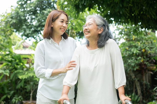 An old elderly Asian woman uses a walker and walking in the backyard with her daughter.
